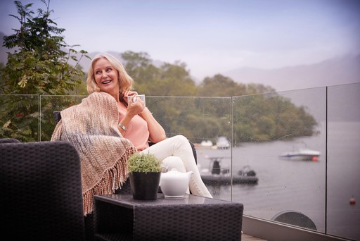 Lady enjoys a drink on the decking of her lodge at Loch Lomond