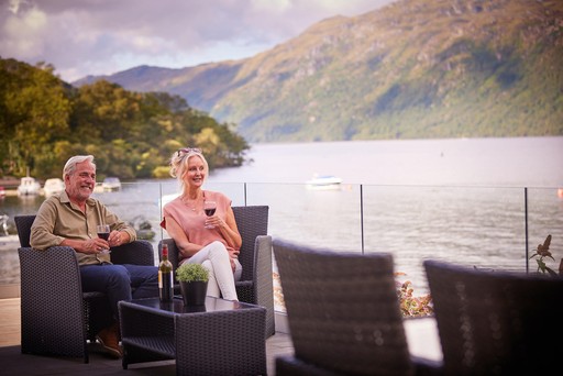 Couple enjoy a drink on the veranda of their lodge at Loch Lomond Holiday Park