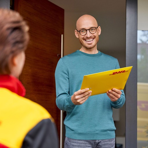 DHL Express courier delivering a yellow-branded envelope to a customer at the doorway of a modern home.