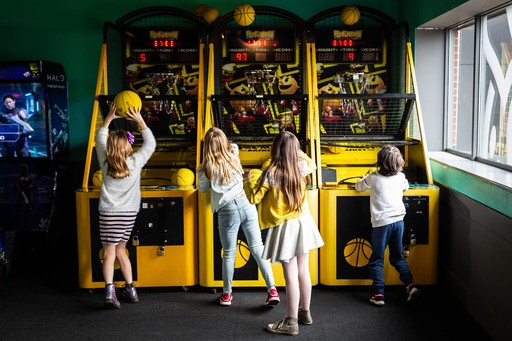 Four young children, 3 girls and 1 boy, playing on a basketball machine in the arcade