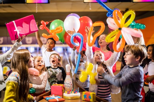 Young children having fun at a bowling birthday party with a birthday cake, presents and balloons